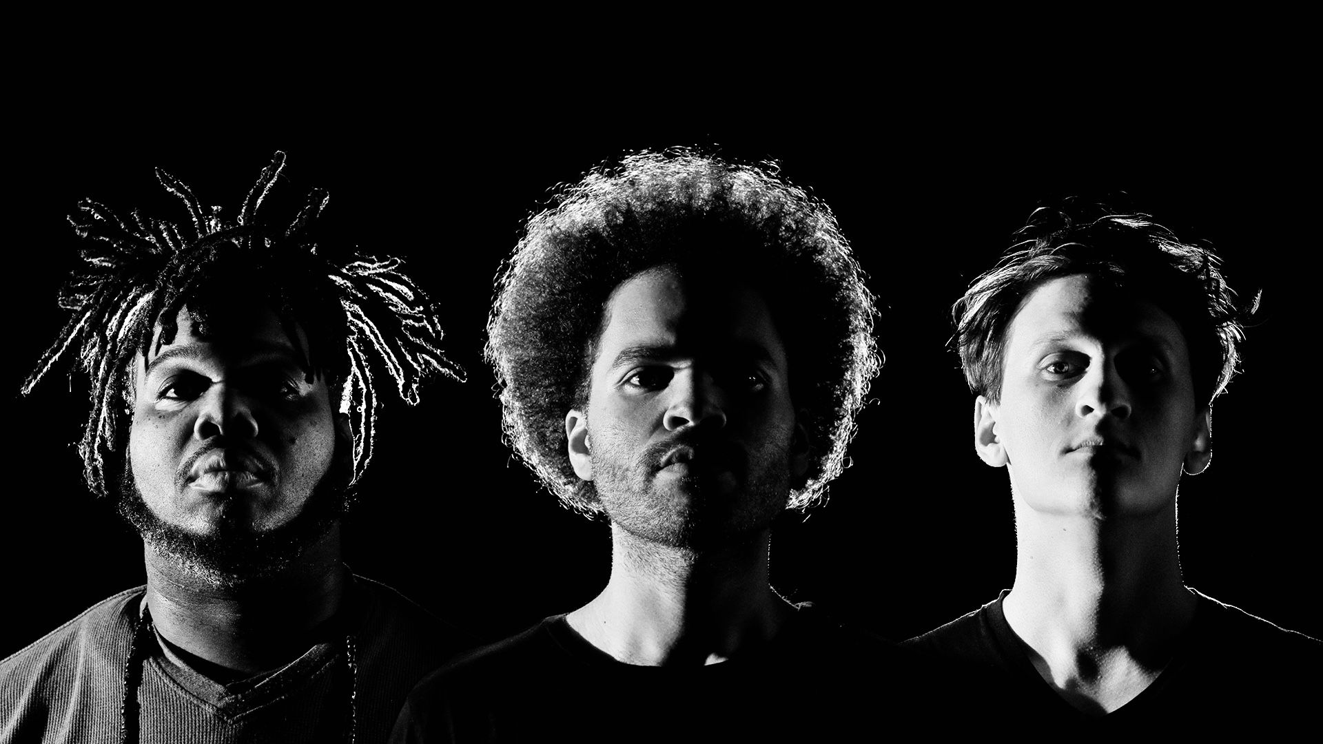 The three members of Hunter-gatherer, backlit against black